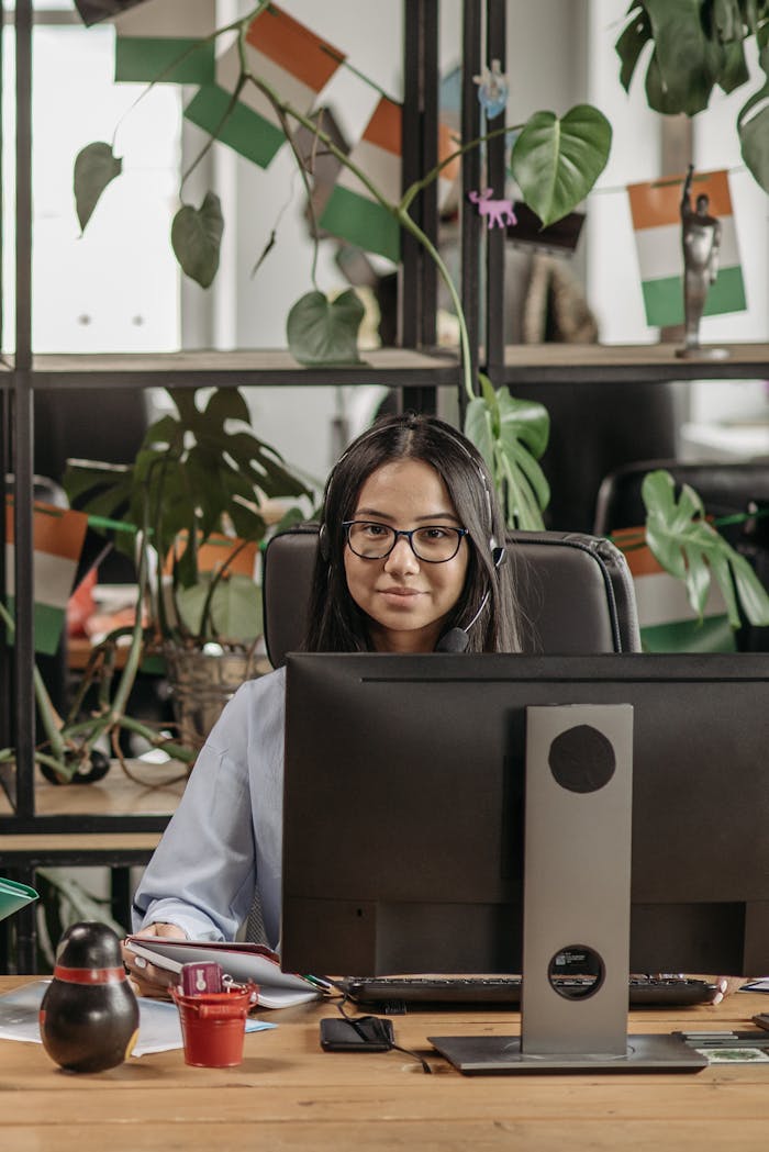 services-02 Asian woman with eyeglasses working at a desk in a modern office, surrounded by plants.