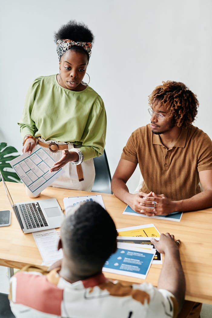 who-we-are High angle view of a diverse team engaged in a collaborative office meeting, discussing documents and using a laptop.
